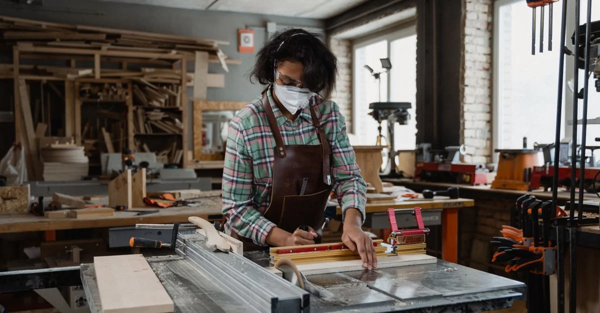 Femme travaillant le bois dans un atelier animé, mettant en avant l'artisanat et l'habileté.
