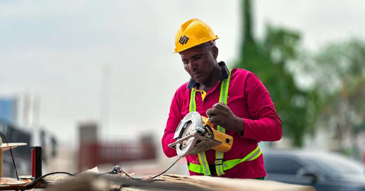 Un ouvrier du bâtiment portant un casque utilise une scie circulaire sur un chantier.