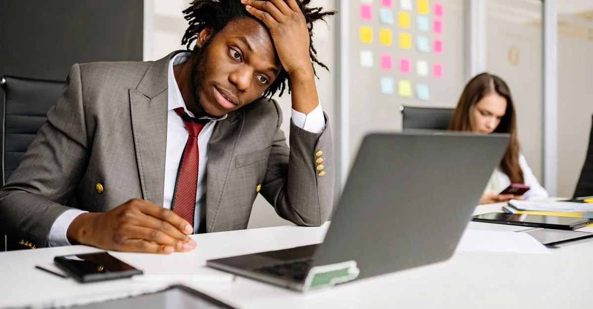 Homme afro-américain stressé au bureau, avec un ordinateur portable et un smartphone sur le bureau.